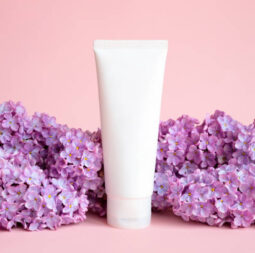 White squeeze bottle tube for branding of medicine or cosmetics - cream, gel, skincare, moisturizer. Cosmetic blank bottle mockup and lilac flowers on pink background. Front view.