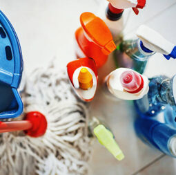 Closeup top view of unrecognizable home cleaning products with blue bucket and a mop on the side. All products placed on white tiled bathroom floor.